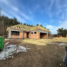 Budowa domu z cegły, widoczny szkielet dachu, drewno budowlane, zielony kontener.
