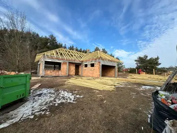 Budowa domu z cegły, widoczny szkielet dachu, drewno budowlane, zielony kontener.